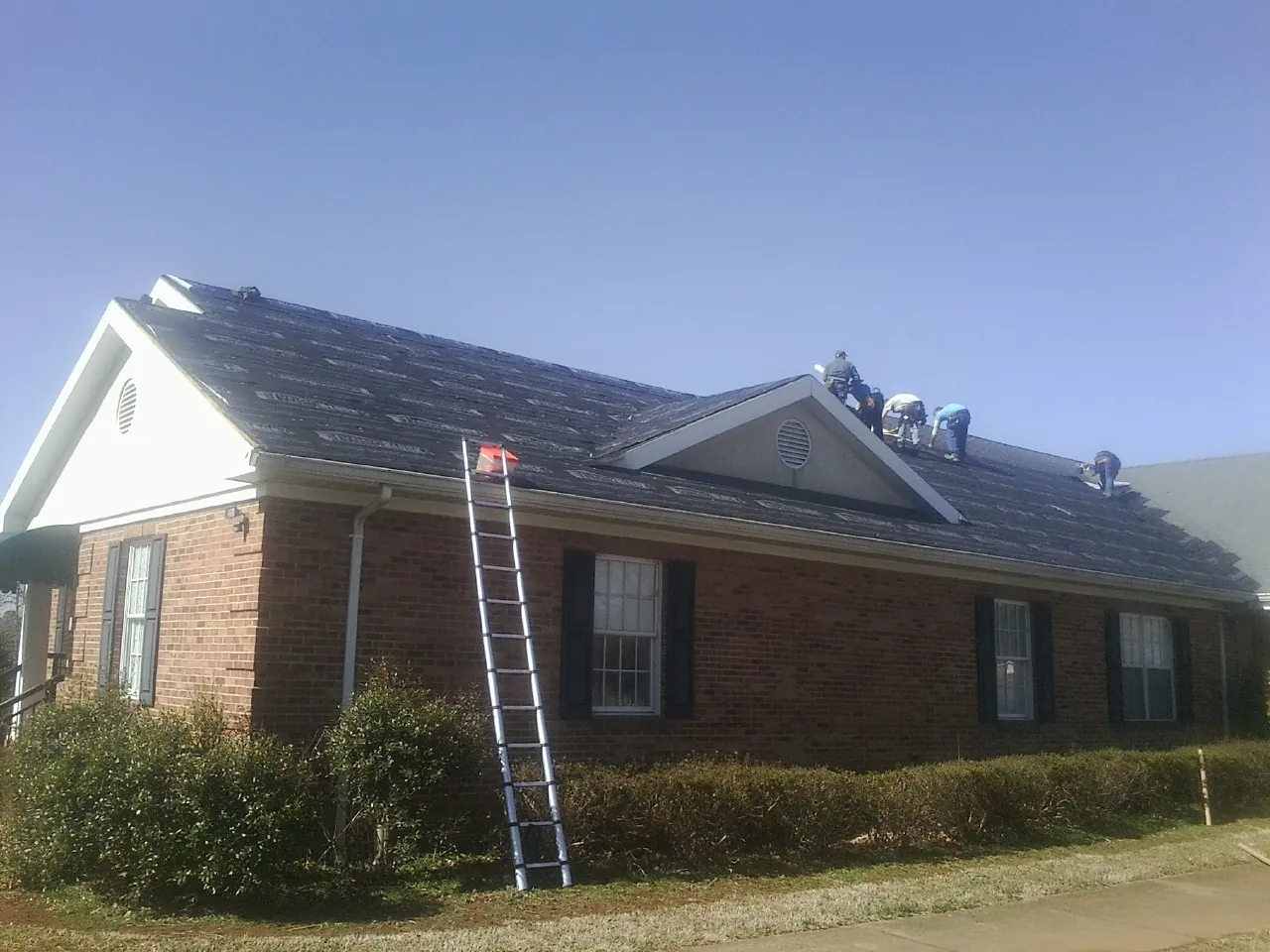 Crew tearing shingles off a brick ranch roof with a ladder set — Emergency Roof Repair work by our crew in Lynn