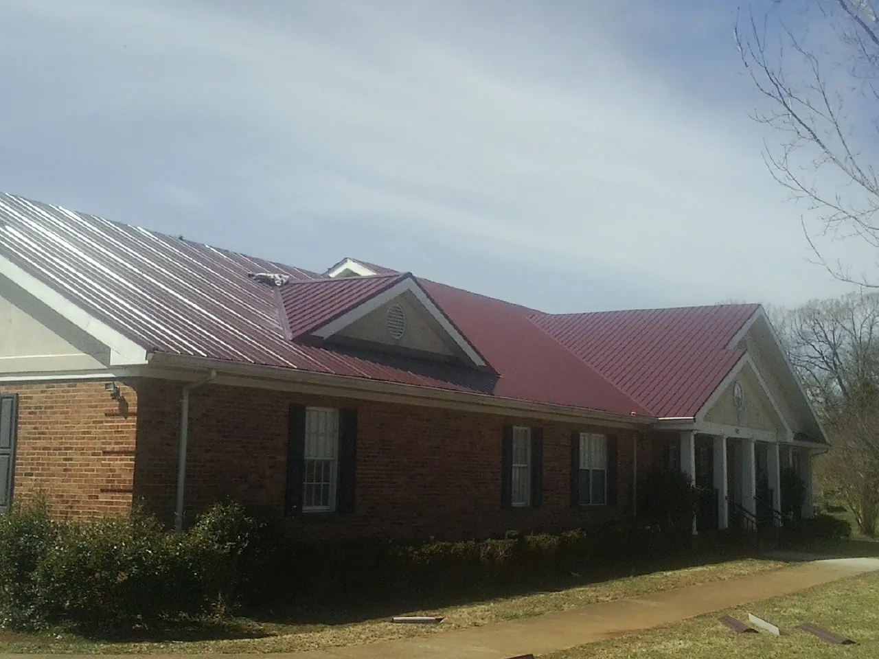 Red metal roof with gabled entries on a long brick building, from a Hail Damage Roof Repair job in Lynn
