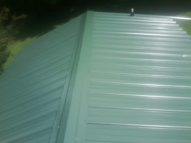 New green metal panels meeting at the ridge of a roof — Flat Roof Repair work by our crew in Lynn
