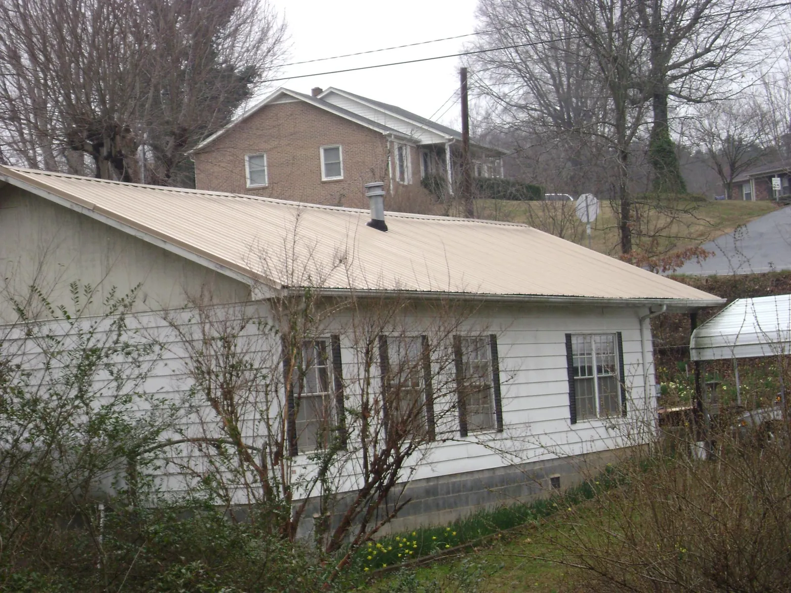 Tan metal roof on a white sided house set into a hillside — Commercial Roofing by Roofing Brothers in Lynn